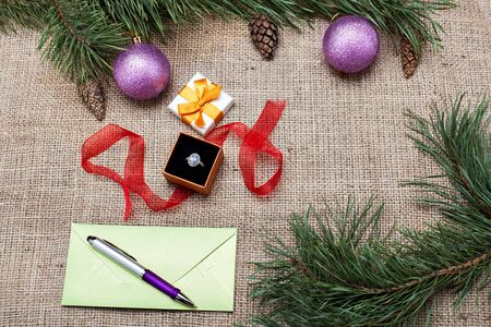 Gift box with a ring and an envelope with a greeting card among Christmas decorations on a burlap backgroundの写真素材