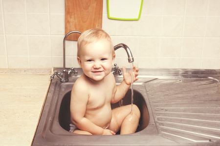 Baby girl sitting in the kitchen sink. She is laughingの写真素材