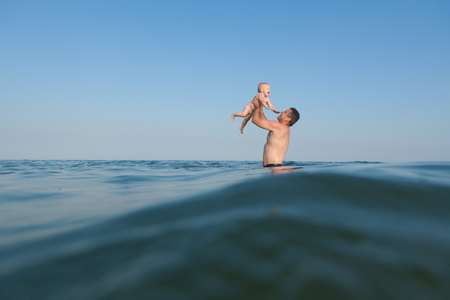 Young dad in the sea playing with his little daughter. He throws up herの写真素材