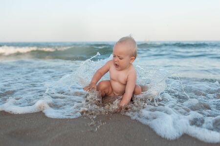 Baby girl playing on the beach among the waves. She opened her mouth in surpriseの写真素材