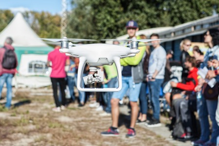 Man controls the copter. People stand around. Focus on the copter, people blurred