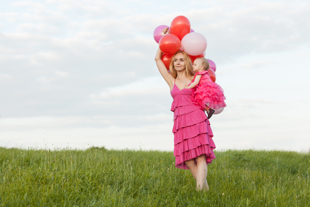 Mom holds a daughter and balloons in her hands. Mom is looking aheadの写真素材