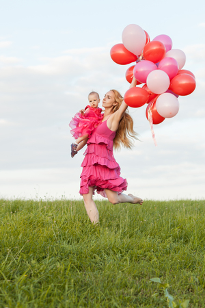 Mom holds a daughter and balloons in her hands and runs along the grassの写真素材