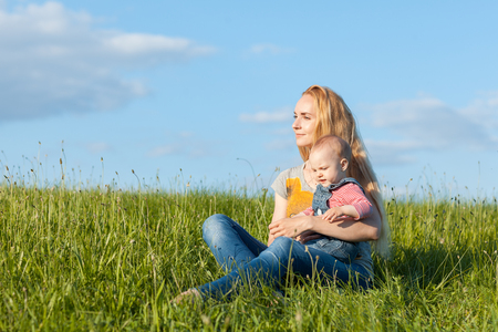 Young mother sitting in the grass and holding a childの写真素材