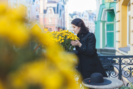 Young woman in a black coat sniffing yellow flowers on the street.の写真素材
