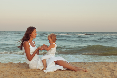 Mom and daughter are sitting on the sand on the beach near the seaの写真素材