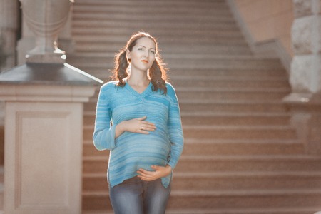 Pregnant woman standing on the stairs, she put her hands on her stomach.の写真素材