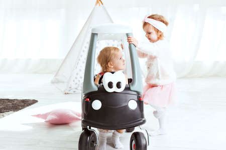 Little cute girl sitting in a toy car, her friend is standing by.の写真素材