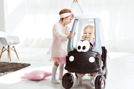 Little girl sitting in a toy car, her friend standing next.の写真素材