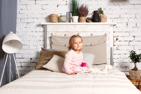 Beautiful girl is sitting on the bed and is holding a toy.の写真素材