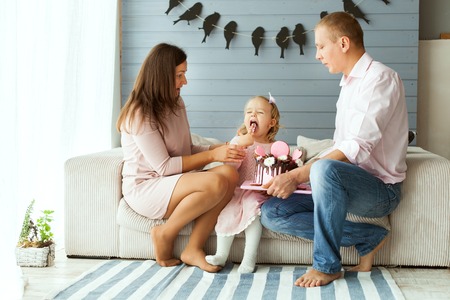 Parents give their daughter a cake. Girl is trying the cake with her fingerの写真素材