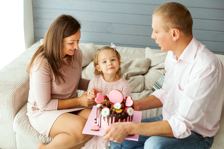Young parents with a daughter. Dad is holding a birthday cakeの写真素材