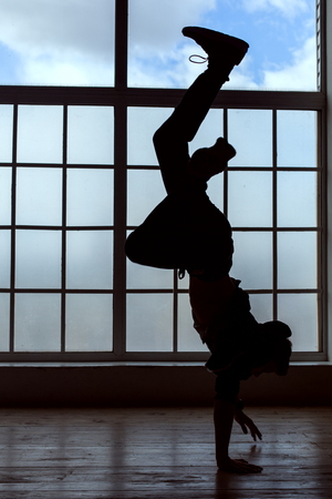 Silhouette of a young man. He makes a stand on his handsの写真素材