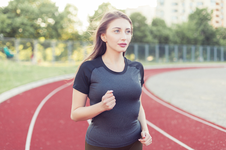 Young beautiful woman in sports uniform runs through the stadium.