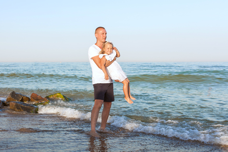 Dad is on the beach and is holding his little daughter in his arms.の写真素材