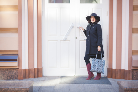 Full young woman in coat and hat standing near the white door.の写真素材