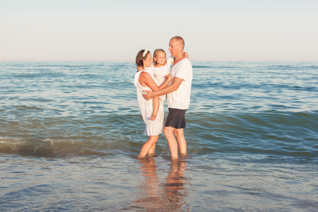 Young parents with a daughter stand on the seashore and embrace.の写真素材