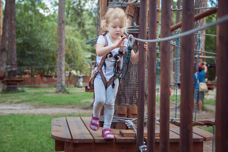 Little girl in the equipment overcomes the obstacle in the rope park.の写真素材