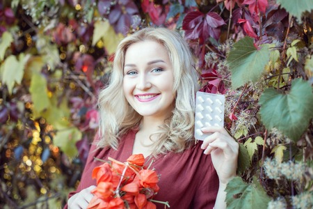 Young woman standing in the autumn park. She is holding a tablet and smiling.の写真素材