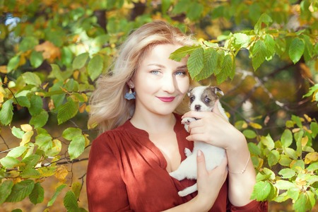 Portrait of a blonde woman with a puppy in autumn park.の写真素材