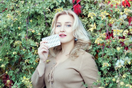Portrait of a beautiful young woman among the bushes with pills in hand.