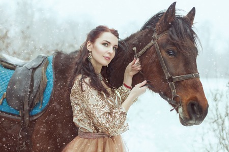 Beautiful young woman stands near the horse. They are in a winter park.の写真素材