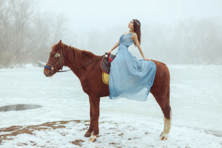 Young beautiful brunette riding a horse by a frozen lake.の写真素材