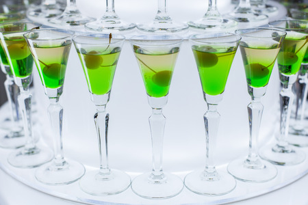 Glasses with a green cocktail and olive stand on the table at a party.の写真素材