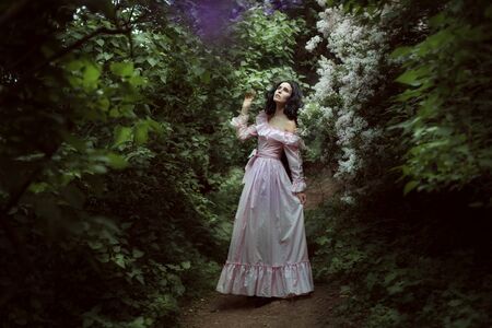 Beautiful brunette woman walks in the spring garden among lilac blossoms.の写真素材