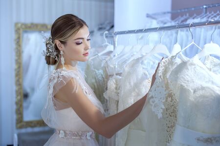 Young beautiful woman in a wedding dress examines wedding dresses at a counter in the salon.の写真素材