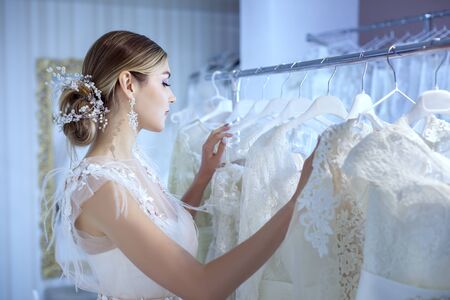 Young beautiful bride in a wedding dress examines wedding dresses at the counter in the store.の写真素材