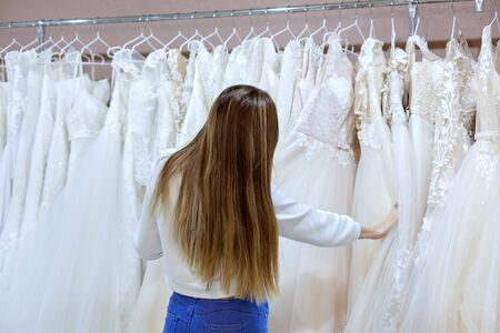 Young beautiful woman in a wedding boutique looks at wedding dresses on a hanger.の写真素材