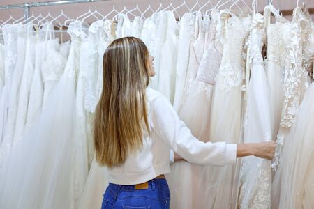 Young woman in a wedding boutique looks at wedding dresses on a hanger.の写真素材