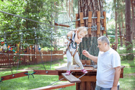 Young dad teaches his daughter to pass obstacles in an amusement parkの写真素材