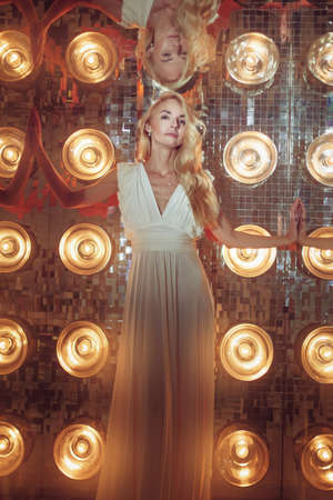 Portrait of a beautiful young woman in a white dress among bright spotlights.の写真素材