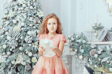Little cute girl stands with a toy angel near the Christmas tree.の写真素材