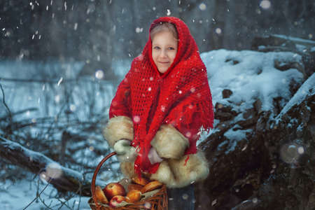 Portrait of a little girl in the winter forest. She has a basket of apples and pies in her hands.の写真素材