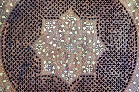 Wooden round table top on Indian market with traditional Indian carving and metal inlay and floral...