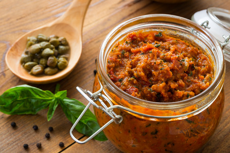 Pesto with dry tomatoes and almonds in a glass jar on a wooden tableの写真素材