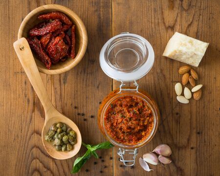 Pesto with dry tomatoes and almonds in a glass jar on a wooden tableの写真素材