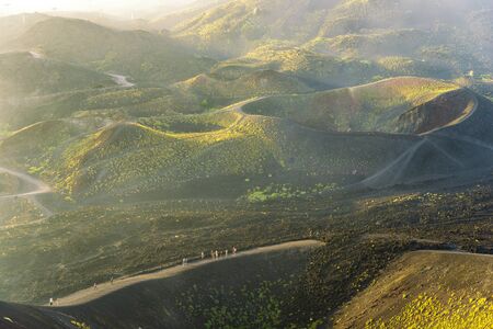 Group of tourists walking on the edge of the crater. Fog at sunset over the volcano Etnaの写真素材