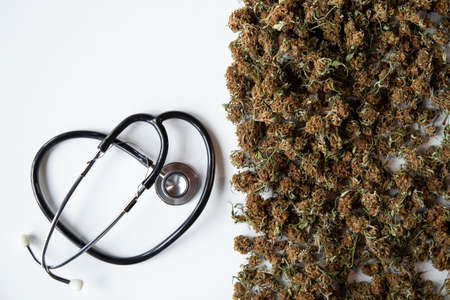 white background with space for copy. on the right side abundant marijuana buds and a heart-shaped stethoscope. medicinal concept.treatment of diseases.の写真素材