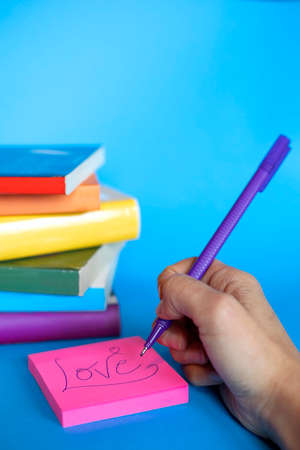 vertical photograph of stacked books with the colors of the lgtb flag and a hand writing love on a...