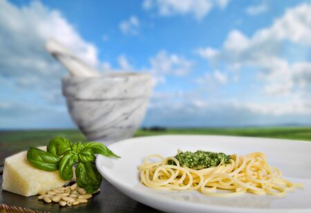 Spaghetti al pesto (a tipical italian basil's sauce), in front of a beautiful italian landscapeの写真素材