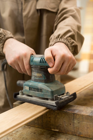 close up of carpenter's hand using a grinder on a wood surface