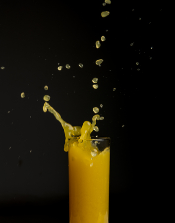 Glass of orange juice with splash, isolated on black backgroundの写真素材
