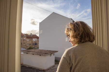 Middle-aged woman at the window with beautiful light of sunsetの写真素材