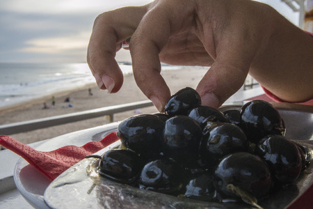 Hand of woman taking an olive from the platter overlooking the seaの写真素材