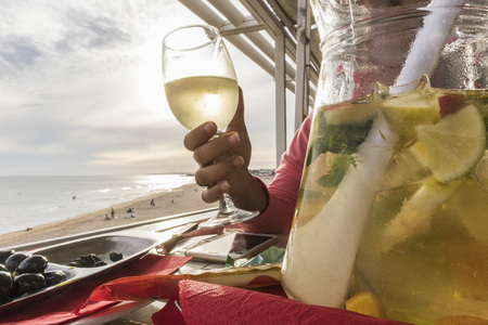 Jug of white sangria with woman hand behind with the beautiful light of the sunset on the beachの写真素材