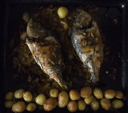 Fish baked in the oven, golden with boiled potatoes and olives in white dish. Typical Portuguese dish.の写真素材